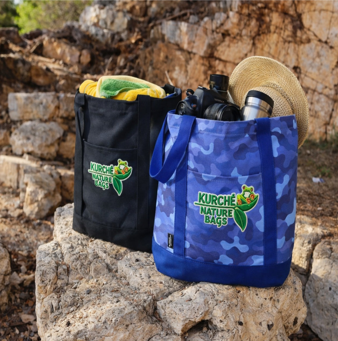Two Kürché Nature Bags reusable canvas tote bags in Midnight Black and Nautical Blue Camo filled with travel gear on rocky outdoor terrain.