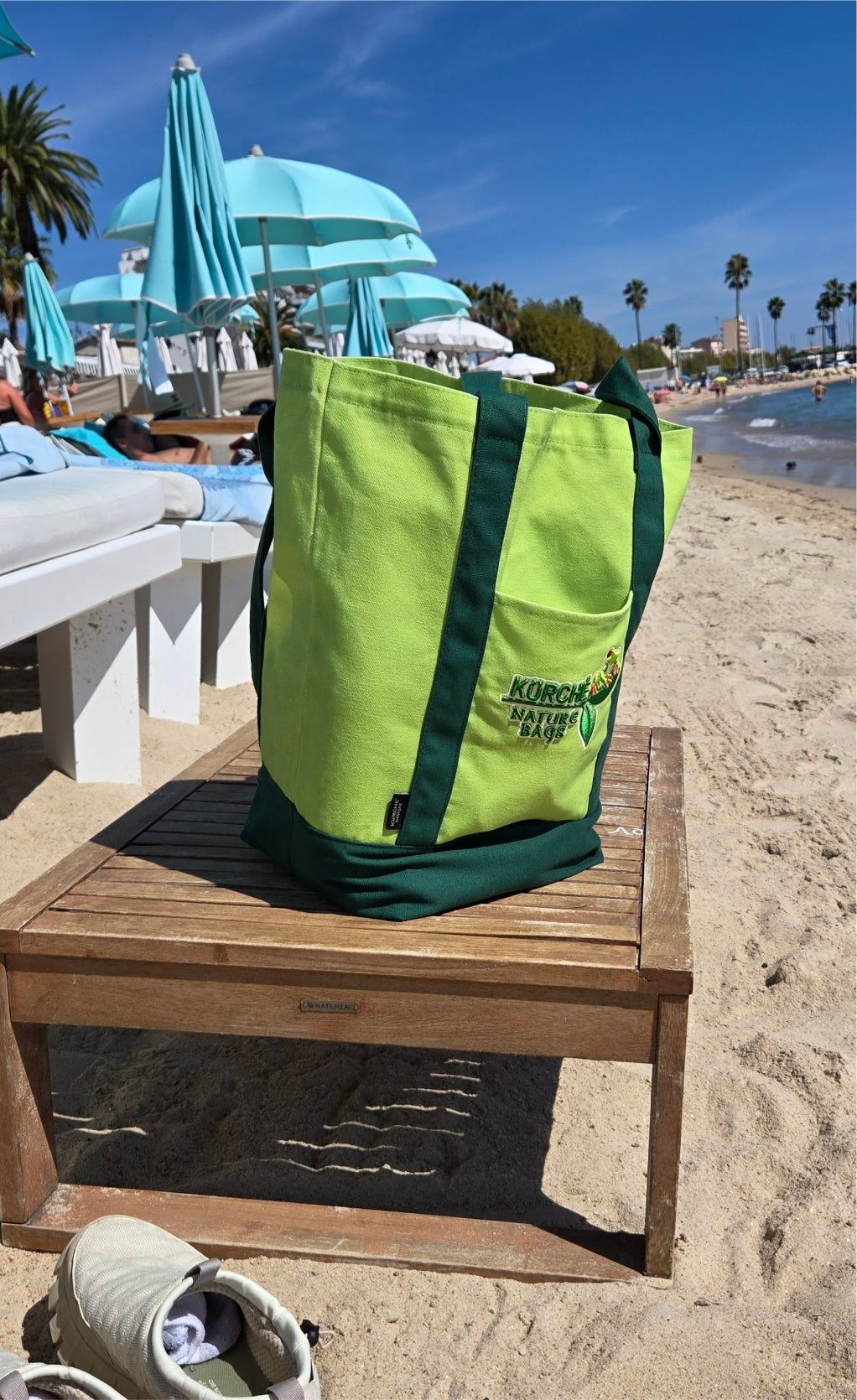 Green Kürché Nature Bags reusable canvas tote bag on a wooden table at a sunny beach